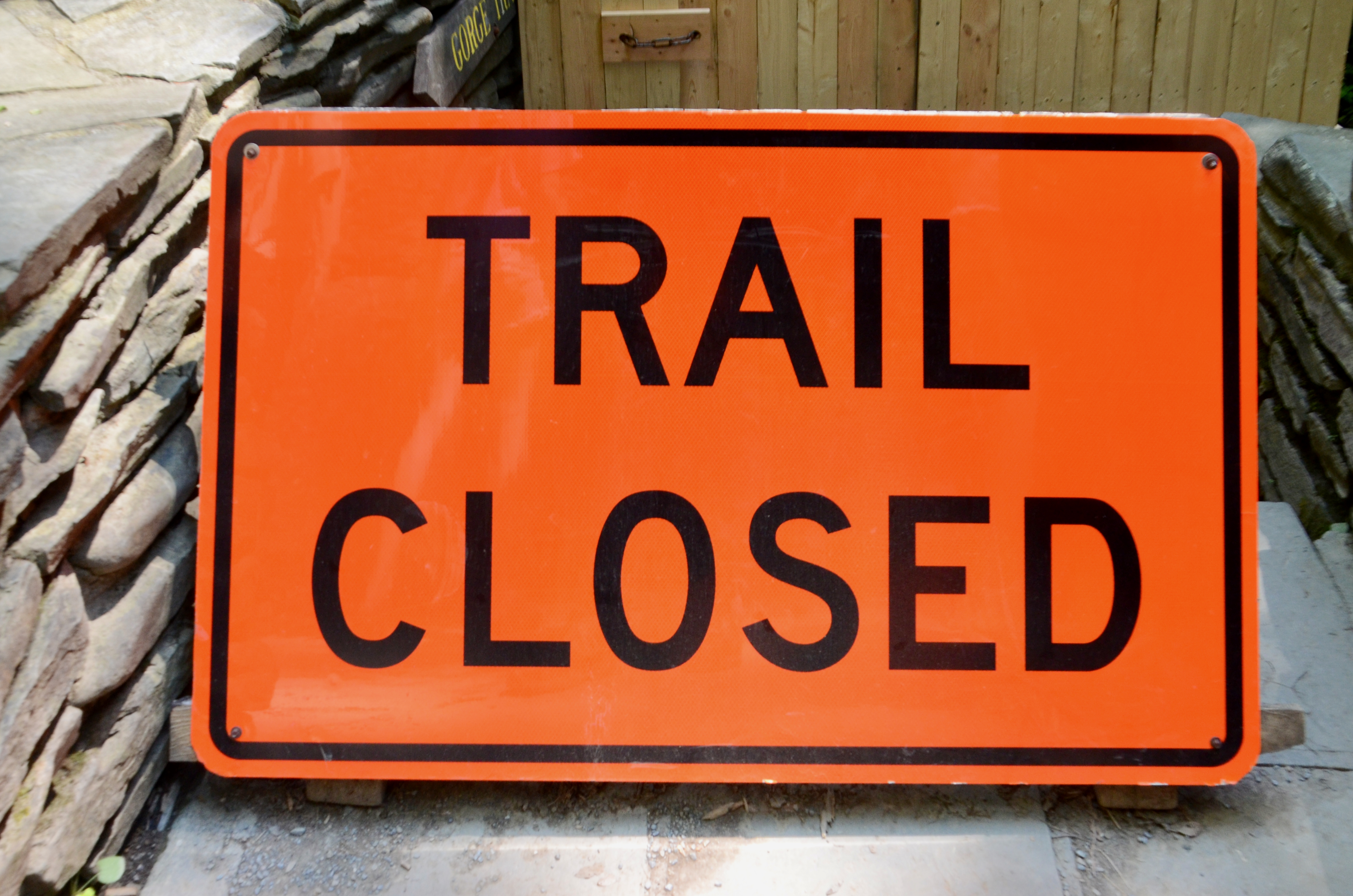 An orange sign sitting on the group that reads Trail Closed.