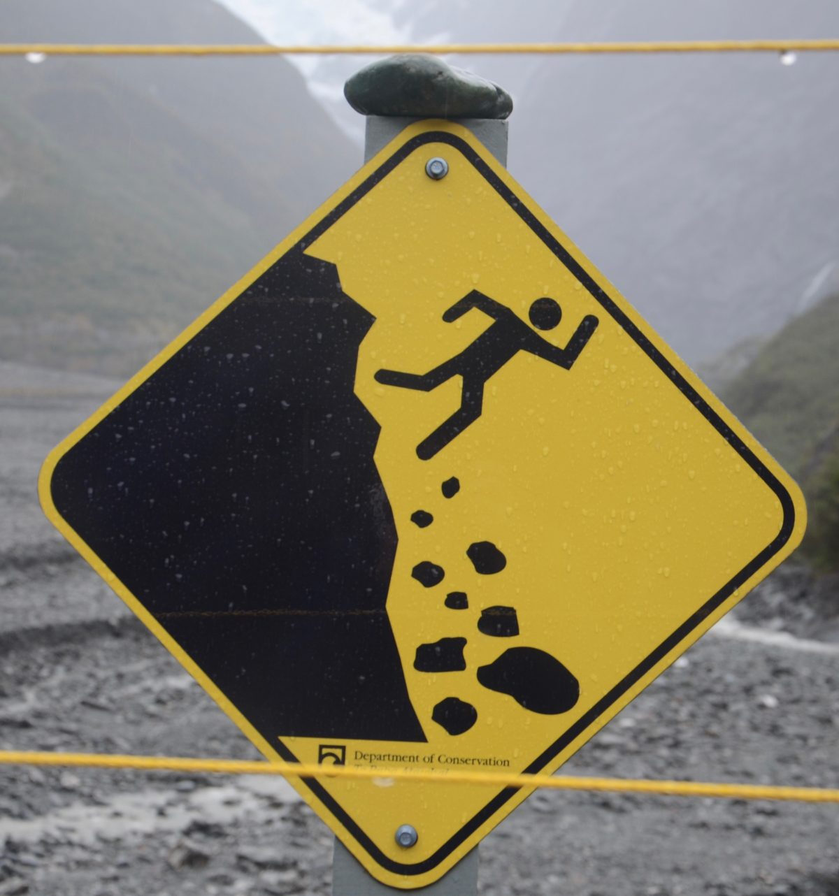 Warning sign of man chasing rocks off a cliff.