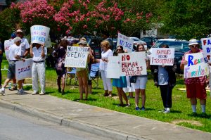 People at the side of the road with signs that read: No Human Being is Illegal. Families belong together. My Family Came as Refugees. No Heat No Ice. Keep Families together. And other slogans.