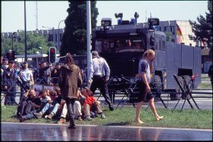 A wet older man standing in front of the water cannon truck with lots of younger people on the ground around him.