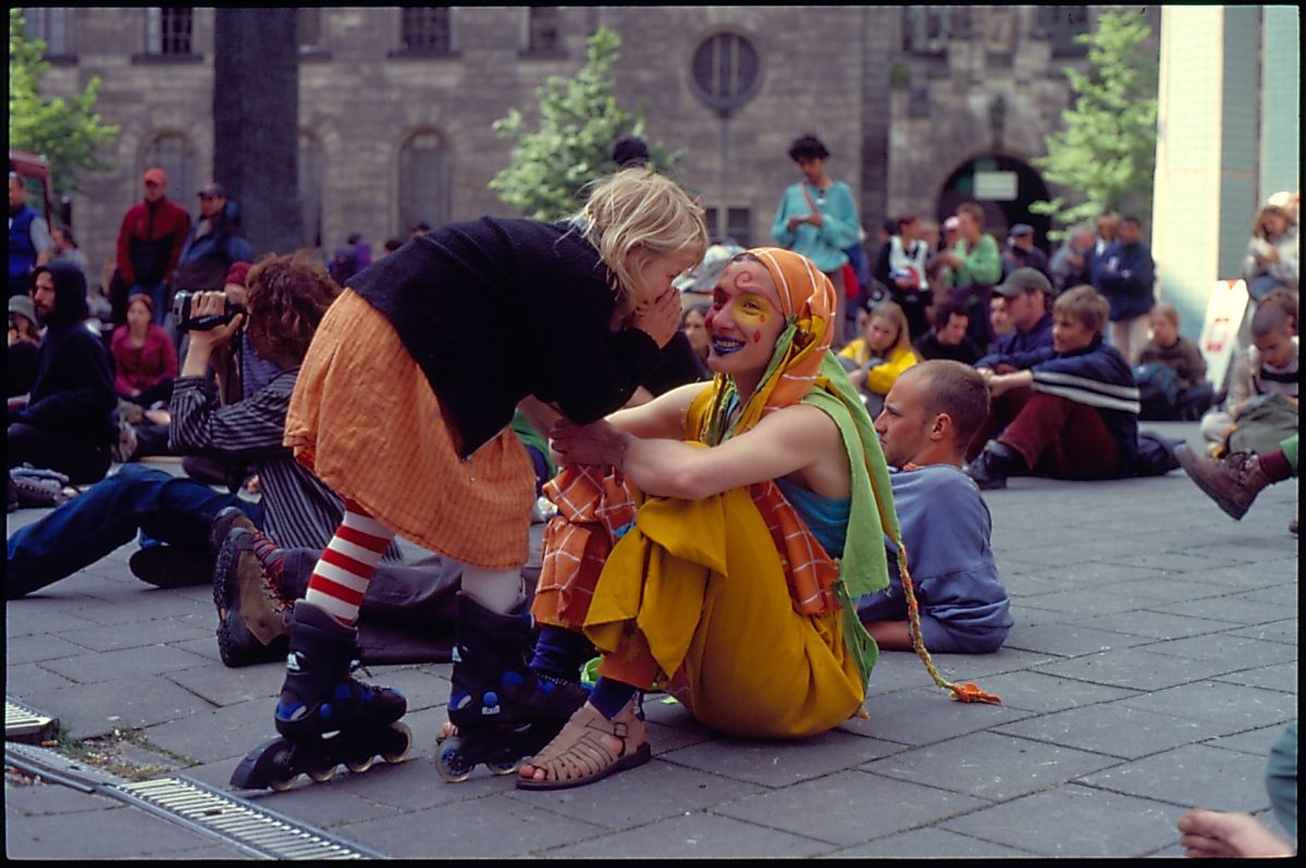 A little girl on rollerblades whispering in her mother's ear, both wearing brightly color outfits.