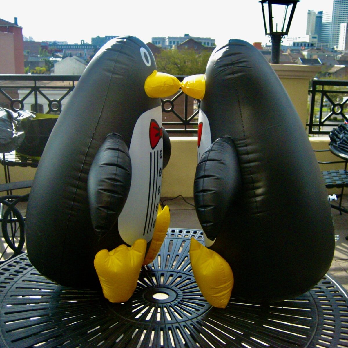 Two inflatable penguins kissing on a table on roof top.