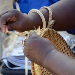 A woman's hands working on making a grass basket.