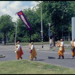 Four monks in orange walking with a banner and drums.