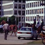 Mounted police walking passed a car and building.