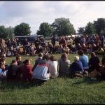 A large group sitting in a field having a meeting.